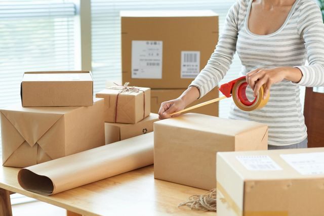 A woman is packing boxes with tape.