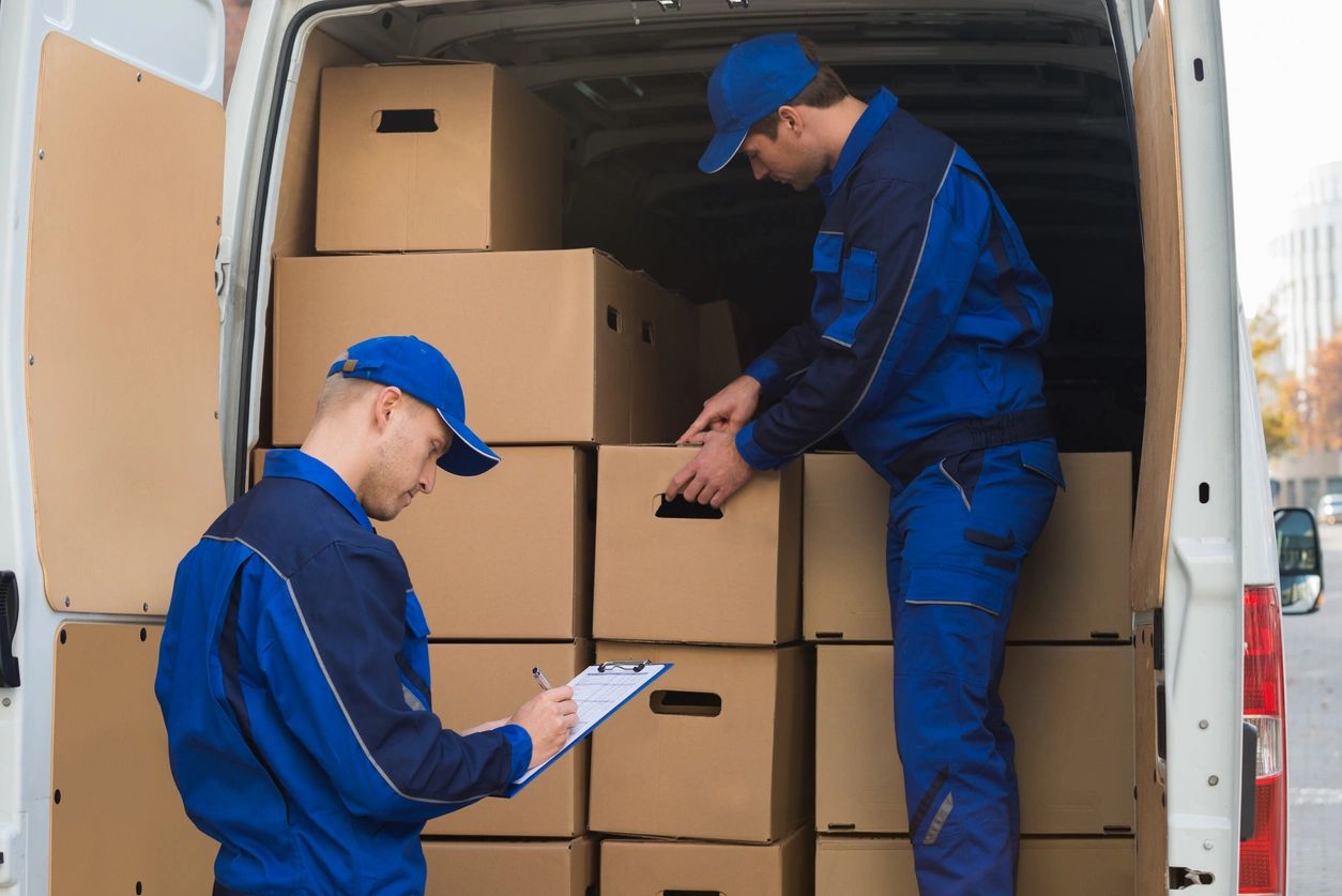 Two men in blue work clothes loading boxes into a truck.