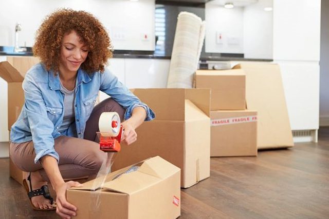 A woman sitting on the floor packing boxes.