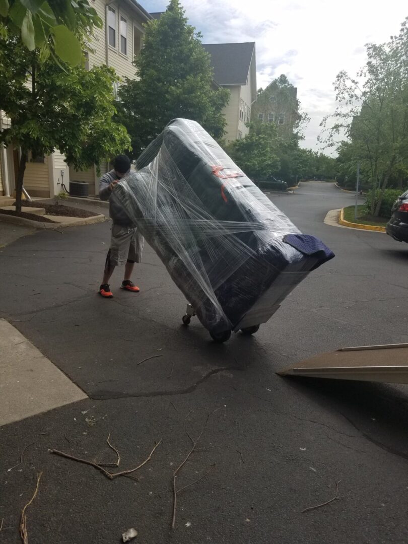 A man pushing a cart with a large piece of furniture on it.