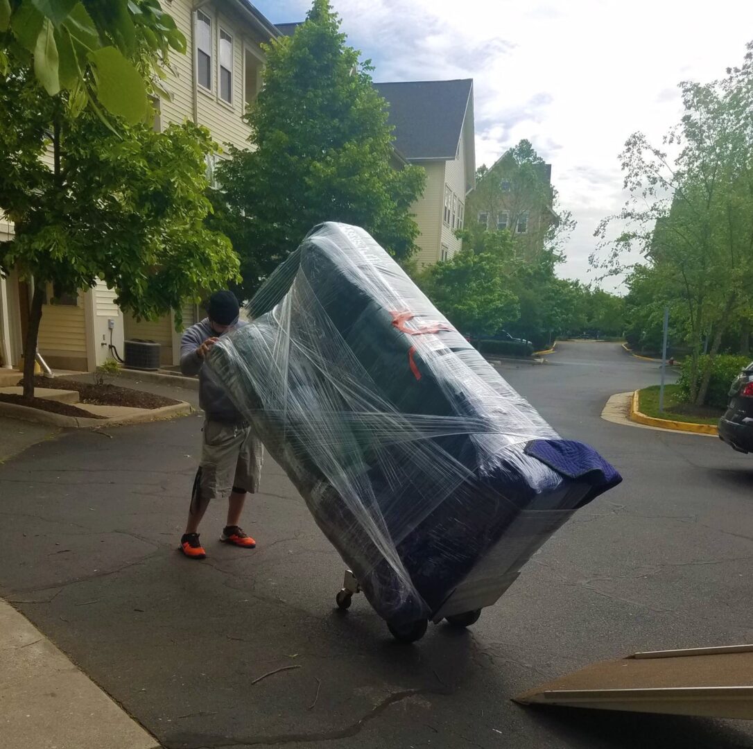 A man pushing a cart with a large piece of furniture on it.